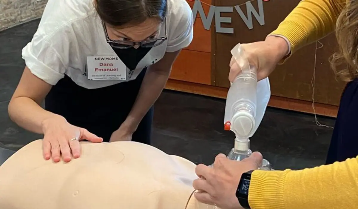 A woman observing another woman performing manual ventilation on a mannequin