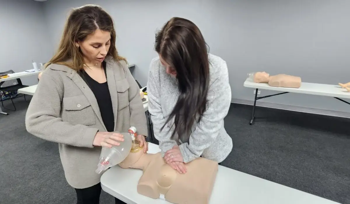 Two women performing CPR training on a mannequin