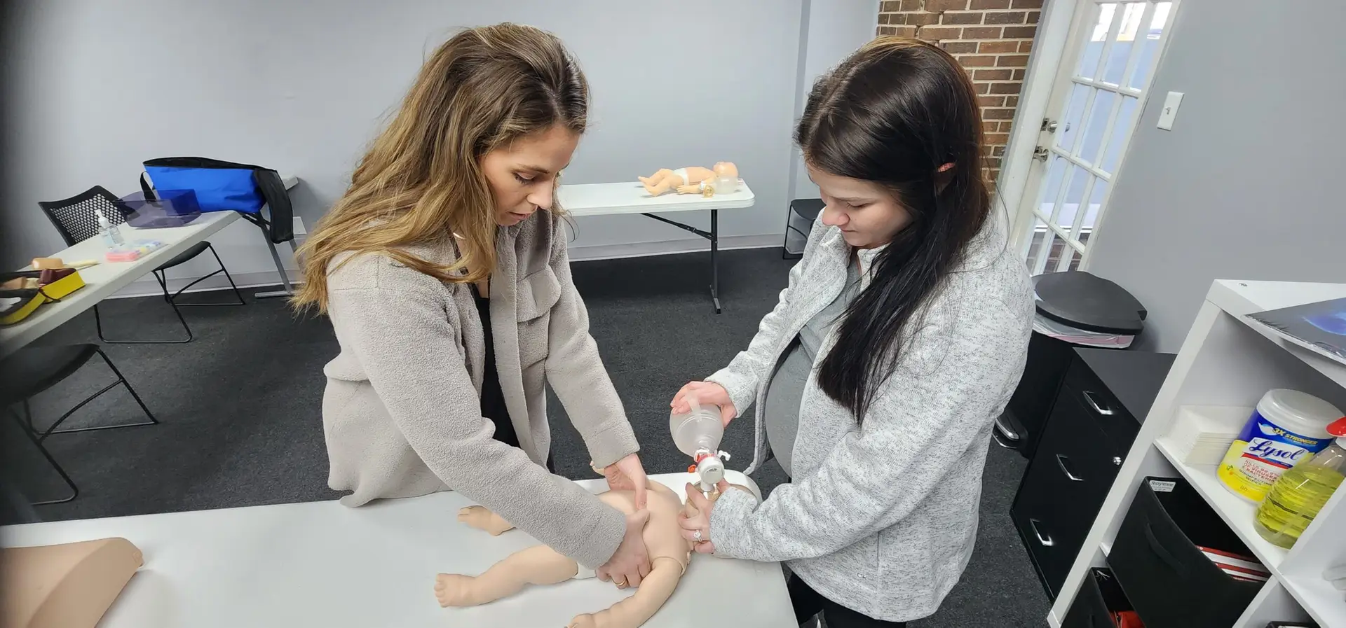 2 women giving CPR to an infant dummy model on a table in the Illinois Safety headquarters in Bolingbrook IL