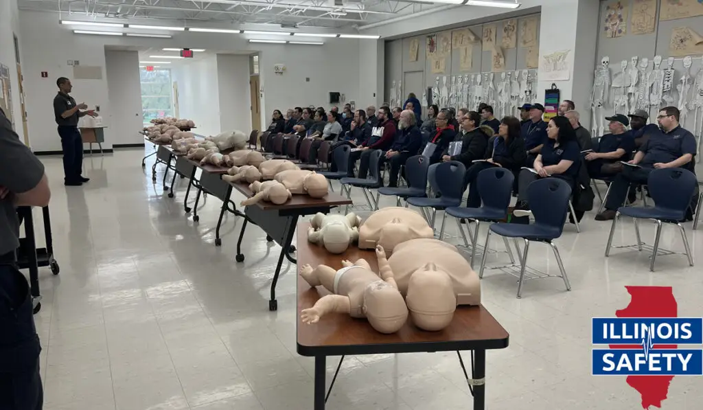 A bunch of people in a room together with the instructor in a CPR class.