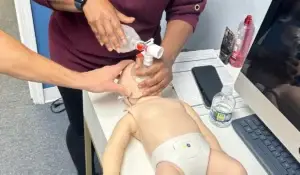 Two individuals perform pediatric airway management using a bag-valve mask on an infant mannequin during PALS certification training.