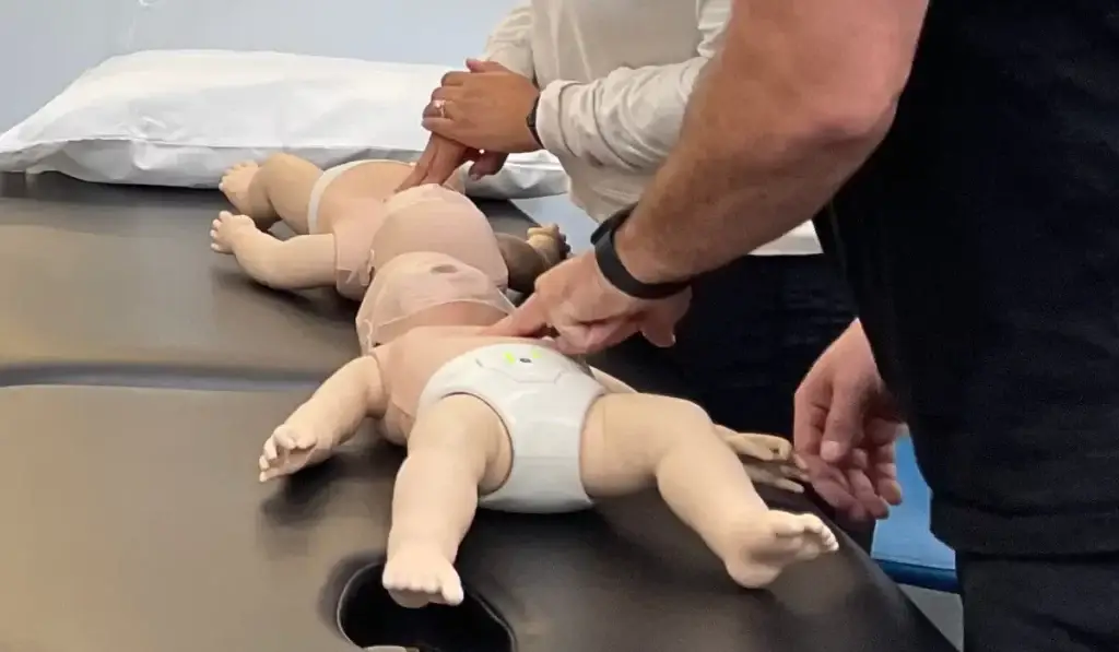Healthcare professionals practicing infant resuscitation techniques on training mannequins during an NRP certification skills session.