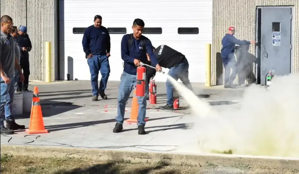 Worker using a fire extinguisher during OSHA emergency plan training drill at a business facility in Elmwood Park.