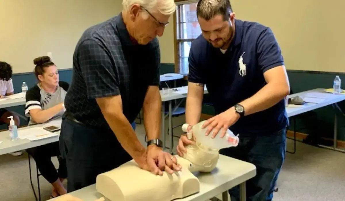 Two instructors demonstrate CPR certification techniques using training manikins during a workplace safety course by Illinois Safety in Illinois, 2025.