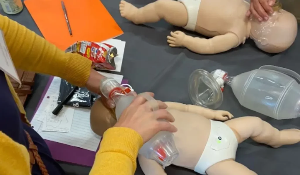 Instructor performing bag-mask ventilation on infant manikin during AHA PALS Certification training in Chicago.