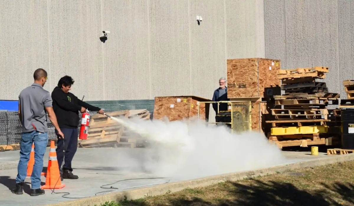 Hands-on outdoor fire extinguisher safety program drill with smoke simulation and staff using real equipment.