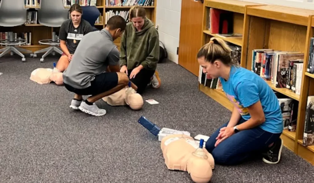 Teachers participating in CPR training for Illinois teachers inside a school classroom setting using pediatric manikins and AED practice equipment